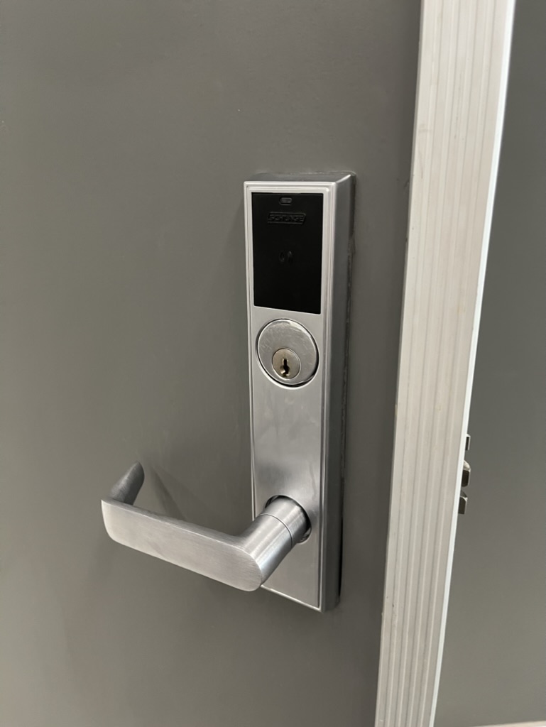 Employee unlocking a glass office door with a phone at a wall-mounted access control reader